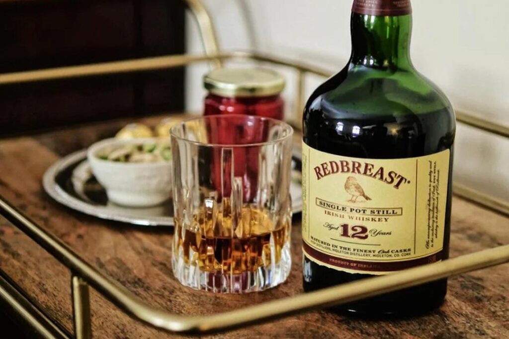 Bottle of Redbreast 12 year old whsikey on wooden table beside drinking glass and snacks