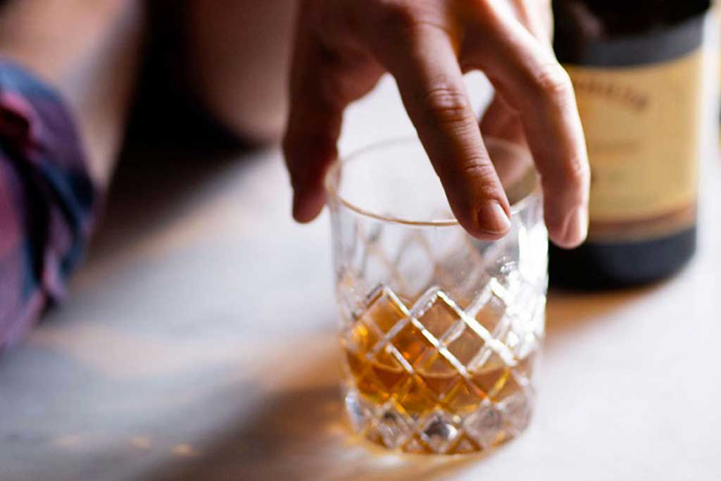 Person touching a drinking glass with bottle of Redbreast whiskey in the background