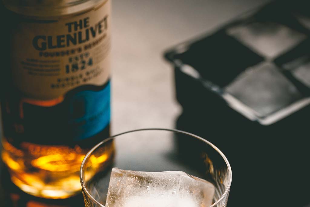 Bottle of Glenlivet Scotch whisky beside drinking glass filled with large chunk of ice