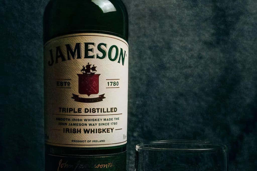 Bottle of Jameson Irish whiskey in dark room beside drinking glass