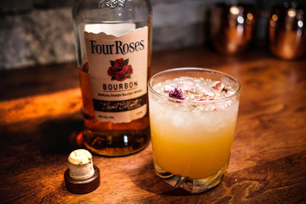 Bottle of Four Roses bourbon beside cocktail glass on wooden table