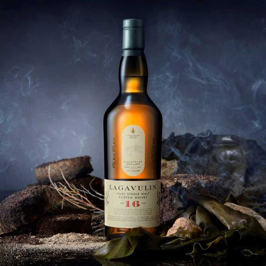 Bottle of Lagavulin whisky beside rocks and seaweed in a dark room