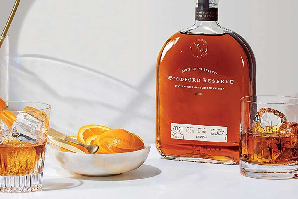 Bottle of Woodford Reserve bourbon beside cocktail equipment and drinking glass