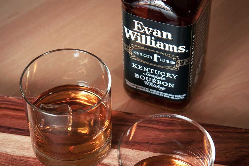 Bottle of black label Evan Williams bourbon sitting beside two drinking glasses