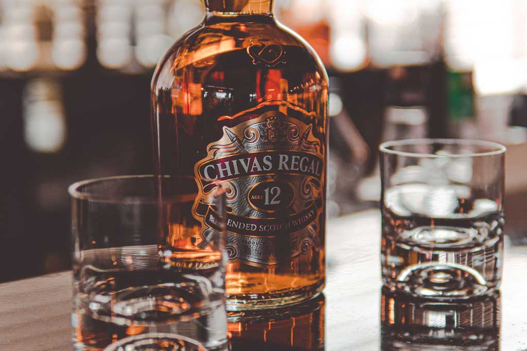 Bottle of Chivas Regal 12 year old whisky on bar top beside drinking glasses
