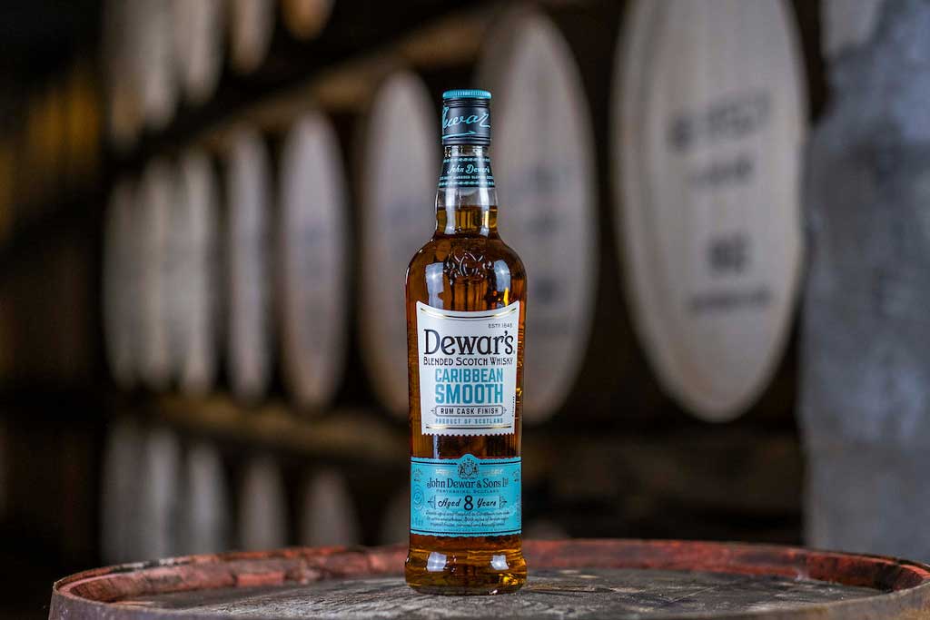 Bottle of Dewar's Caribbean Smooth whisky on top of cask in dark room