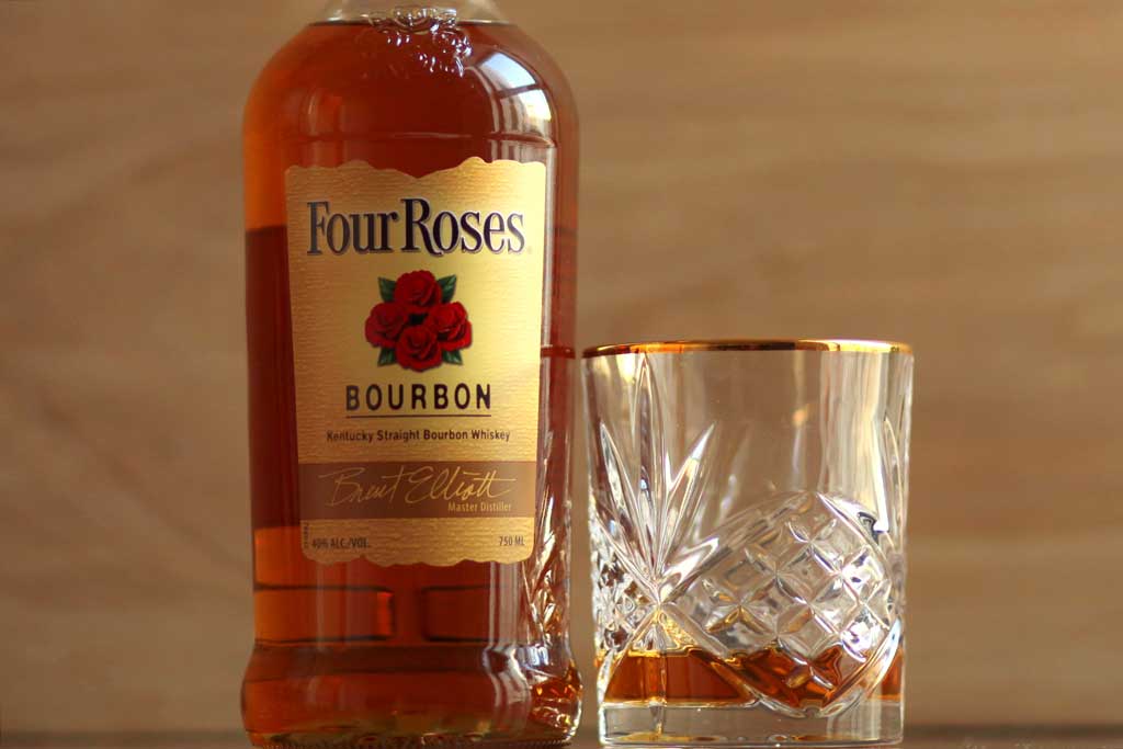 Bottle of Four Roses Yellow Label bourbon beside rocks drinking glass on table