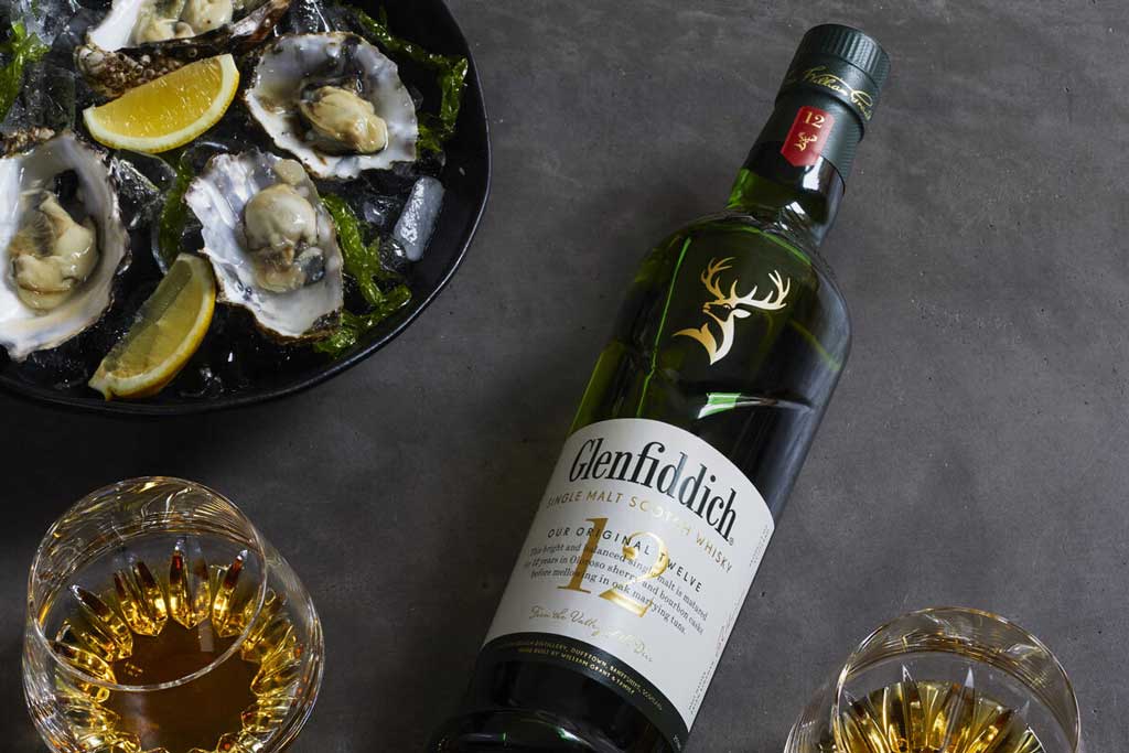 Bottle of Glenfiddich whisky lying beside drinks glasses and ice bowl of oysters