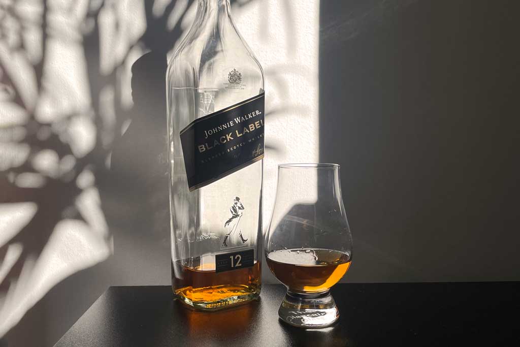 Bottle of Johnnie Walker Black Label in bright sunlight beside Glencairn drinking glass