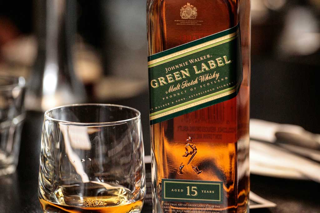 Bottle of Johnnie Walker Green Label whisky beside rocks glass on bar top