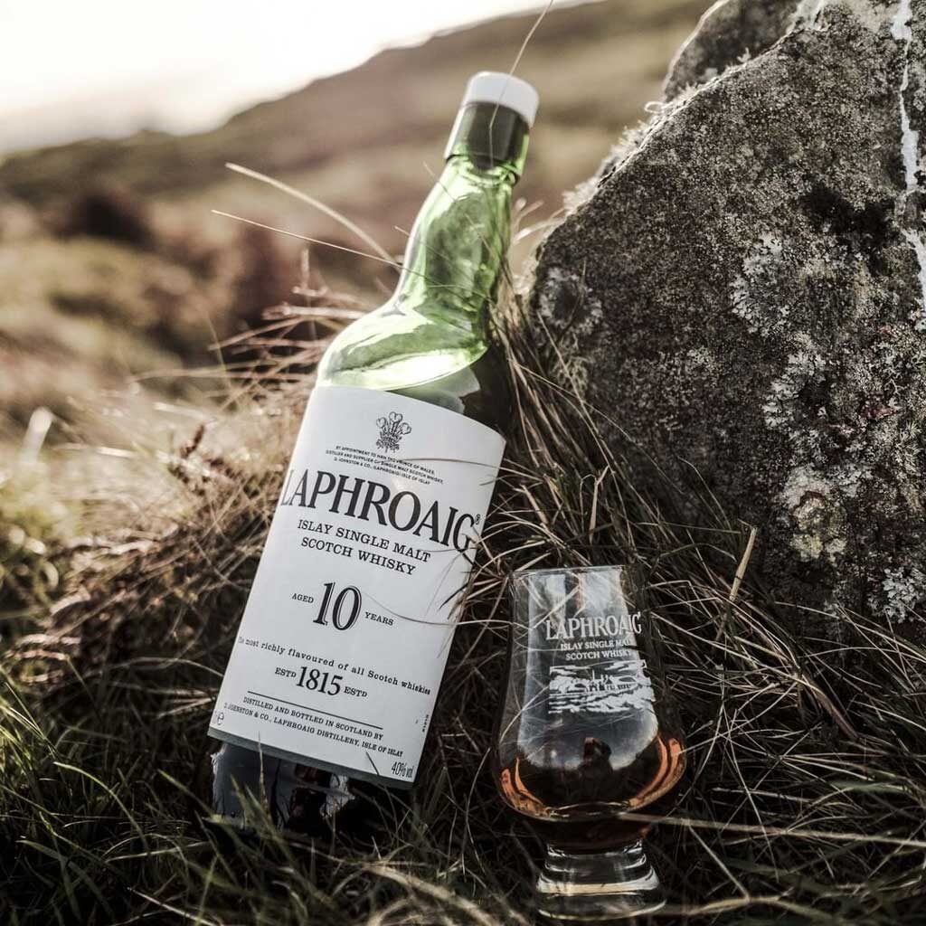 Bottle of Laphroaig 10 year old whisky lying beside Glencairn drinking glass outside in grass