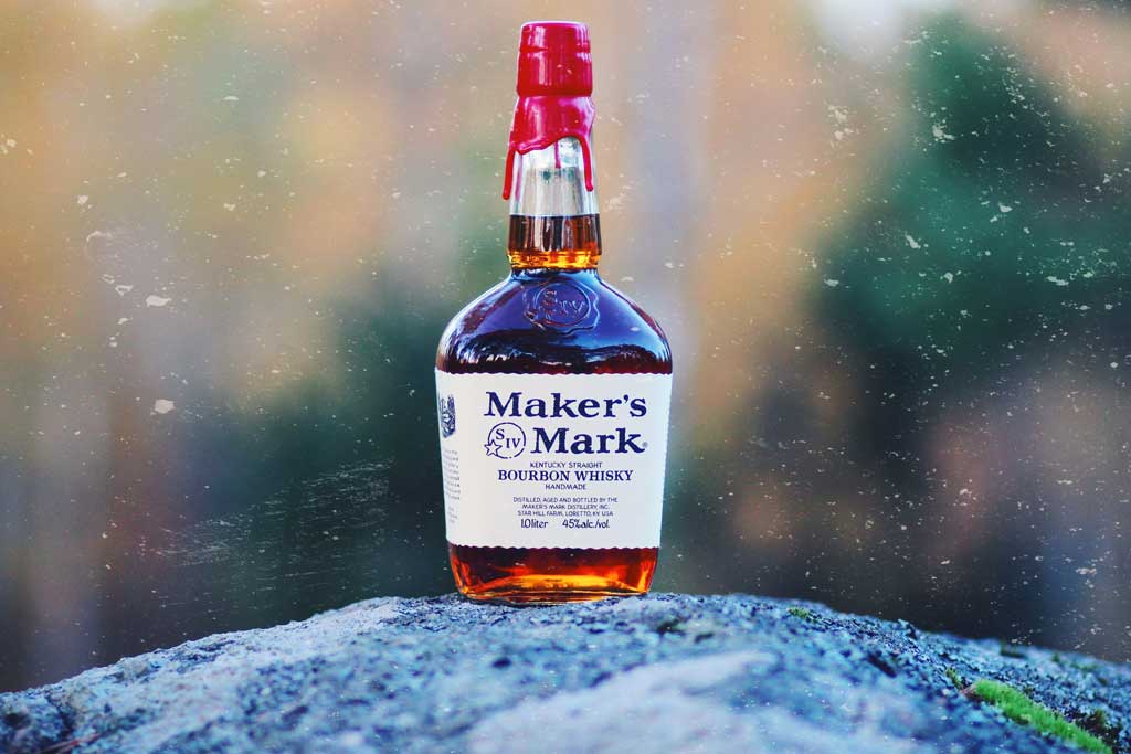 Bottle of Makers Mark bourbon resting on top of rock outside