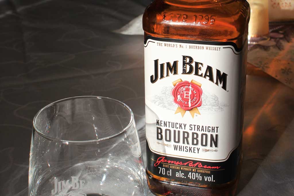 Close view of Jim Beam bourbon bottle beside drinking glass