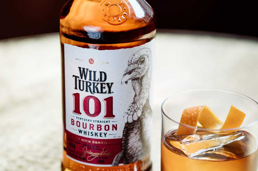 Close view of Wild Turkey 101 proof bourbon bottle beside Old Fashioned cocktail