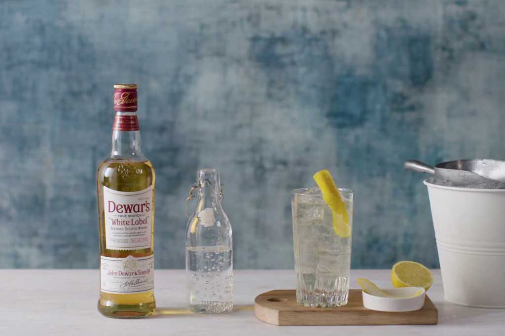 Dewars White Label whisky on table beside highball cocktail glass and ice bucket