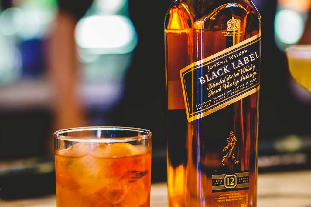 Johnnie Walker Black Label whisky beside a rocks drinking glass on bar top