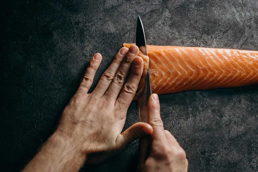 Person slicing smoked salmon fillet with a knife