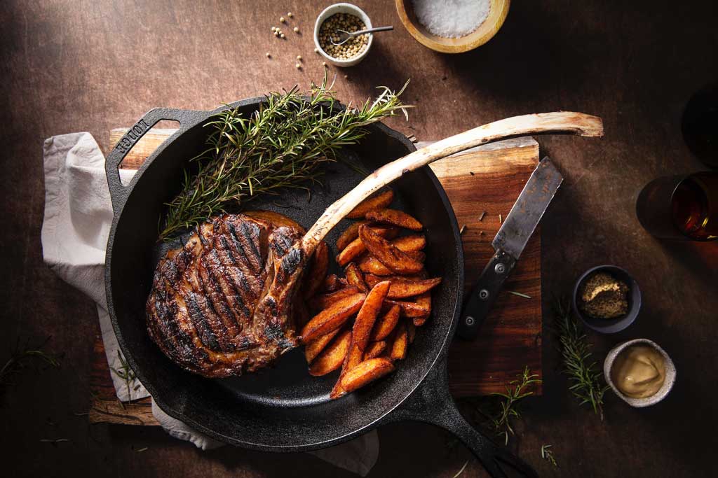 Skillet with steak and carrots inside on top of wooden table