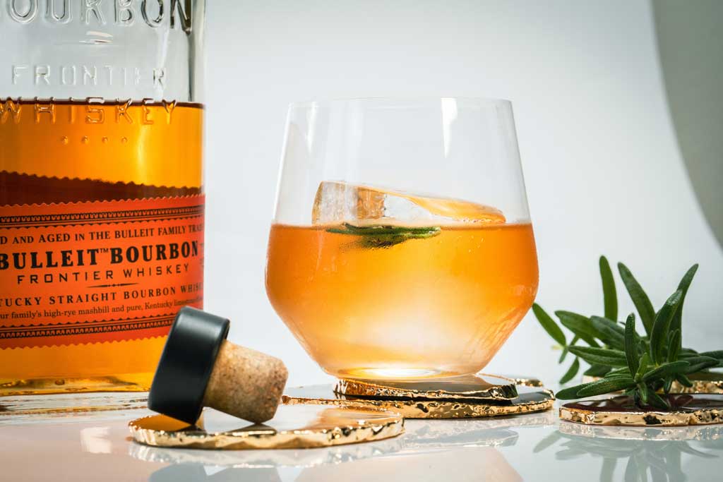 Whisky cocktail beside rosemary sprig and Bulleit Bourbon bottle