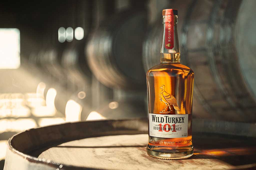 Wild Turkey 101 proof whiskey bottle on top of barrel inside a dark rickhouse 