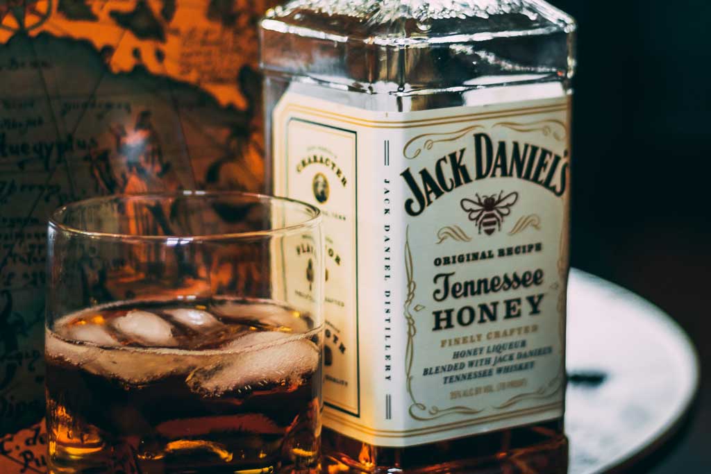 Jack Daniels Honey bottle beside drinking glass