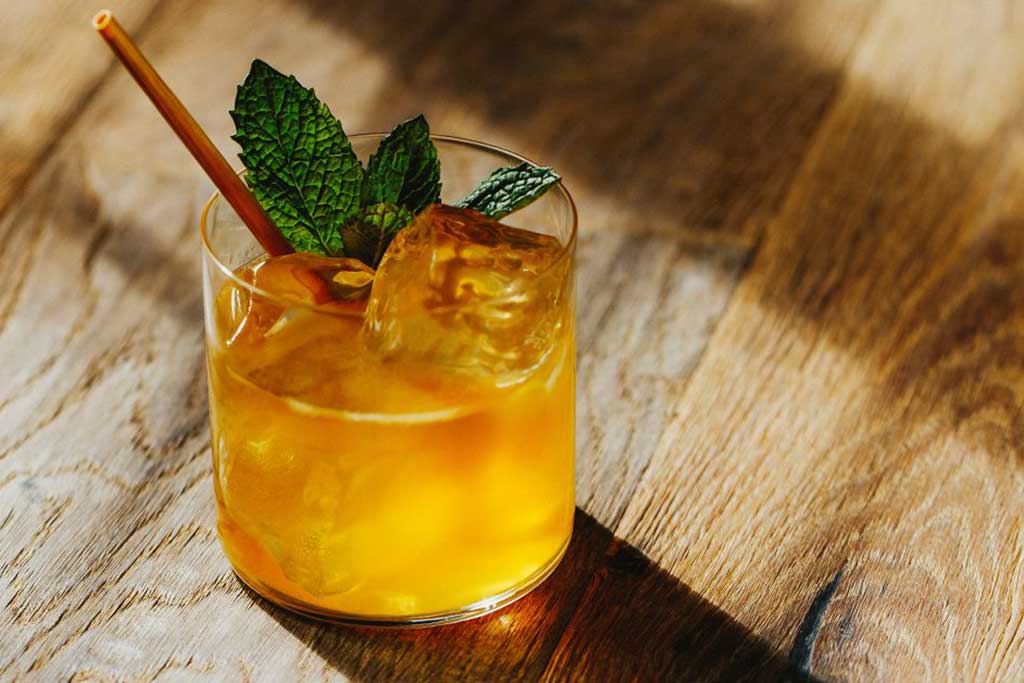 Orange coloured cocktail garnished with mint on wooden table