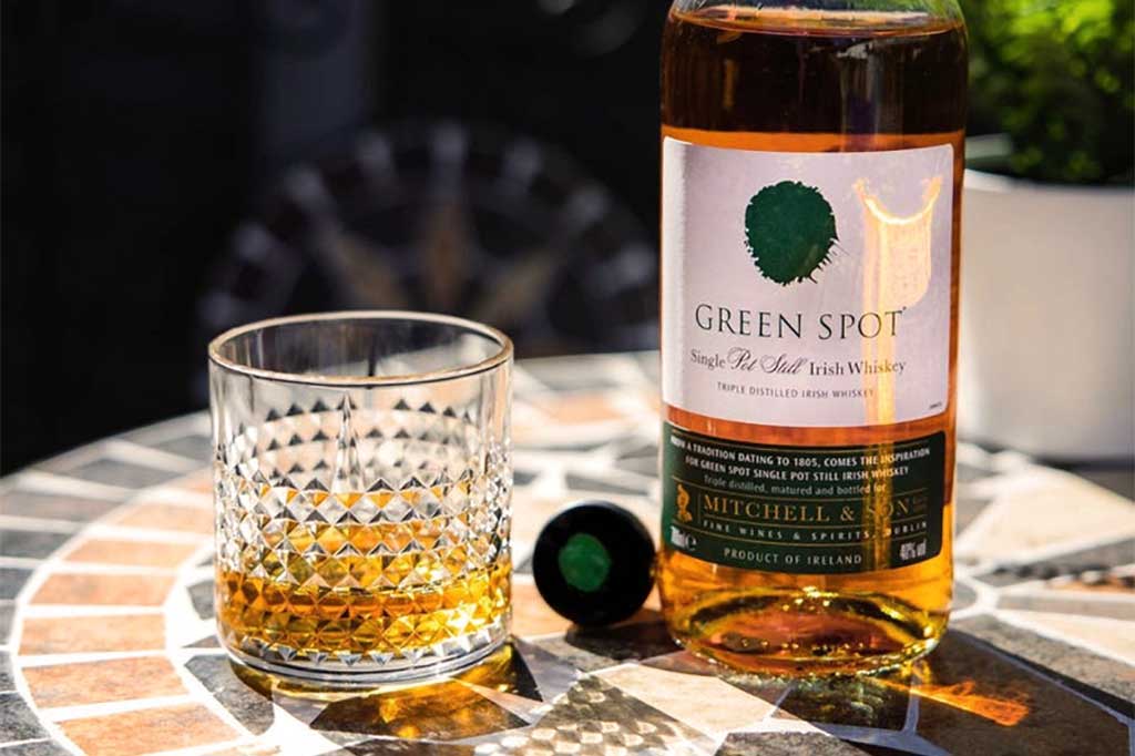 Bottle of Green Spot Irish whiskey on table beside rocks drinking glass