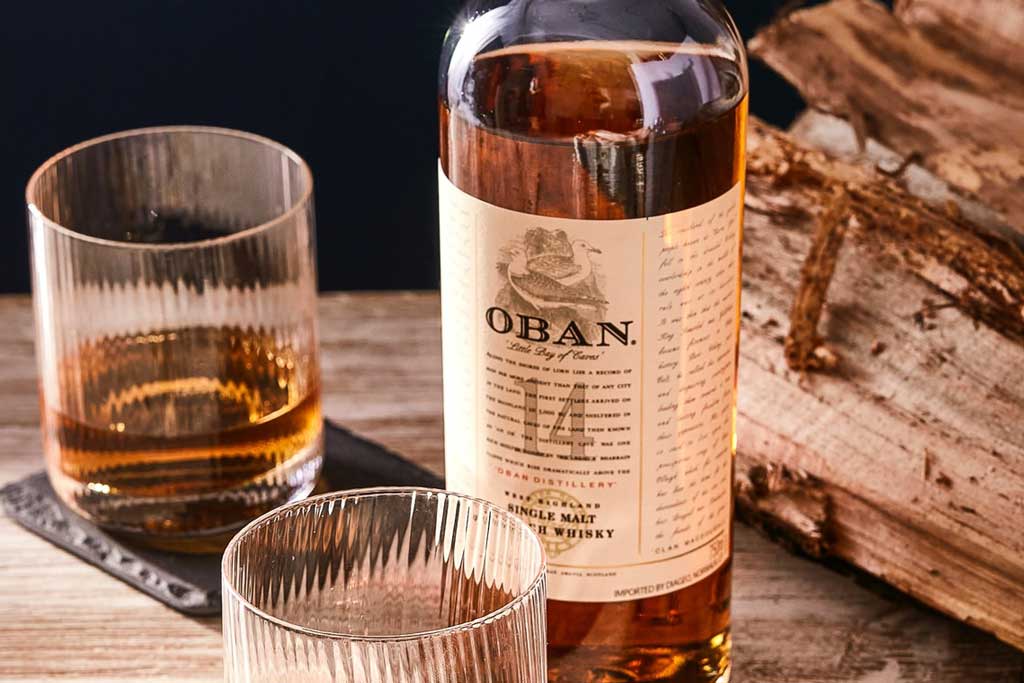 Bottle of Oban 14 year old whisky beside two drinking glasses on table