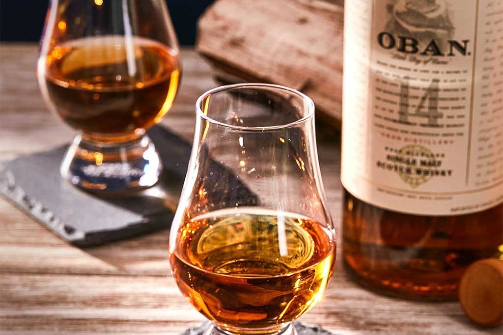 Close view of two Glencairn drinking glasses beside Oban 14 whisky bottle on table