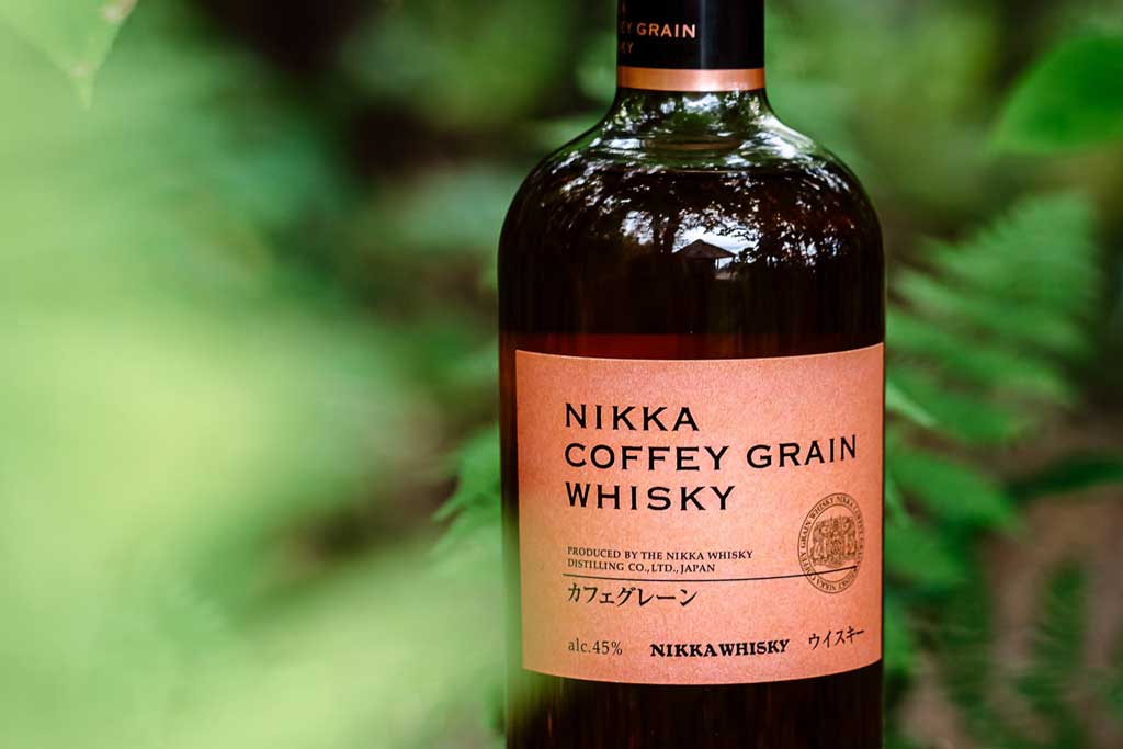 Nikka Coffey Grain whisky bottle beside green garden plants