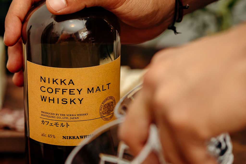 Person holding Nikka Coffey Malt whisky bottle in their hand outside on sunny day