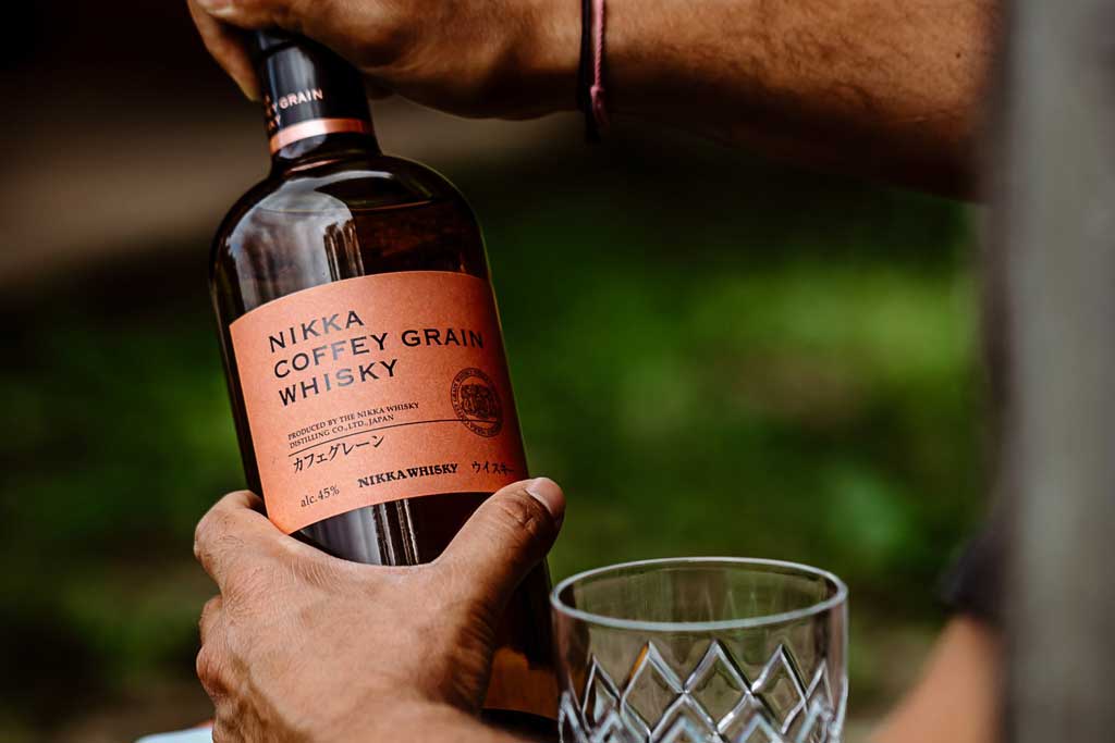 Person opening Nikka Coffey Grain whisky bottle outside on sunny day