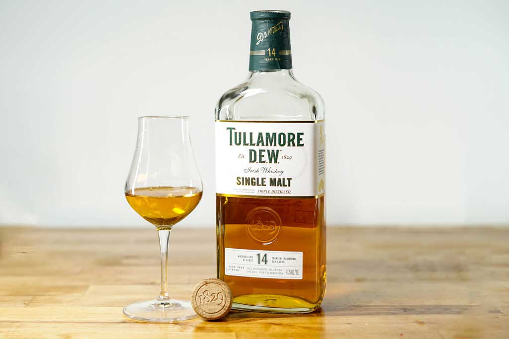 Bottle of 14 year old Tullamore Dew single malt Irish whiskey beside tulip drinking glass