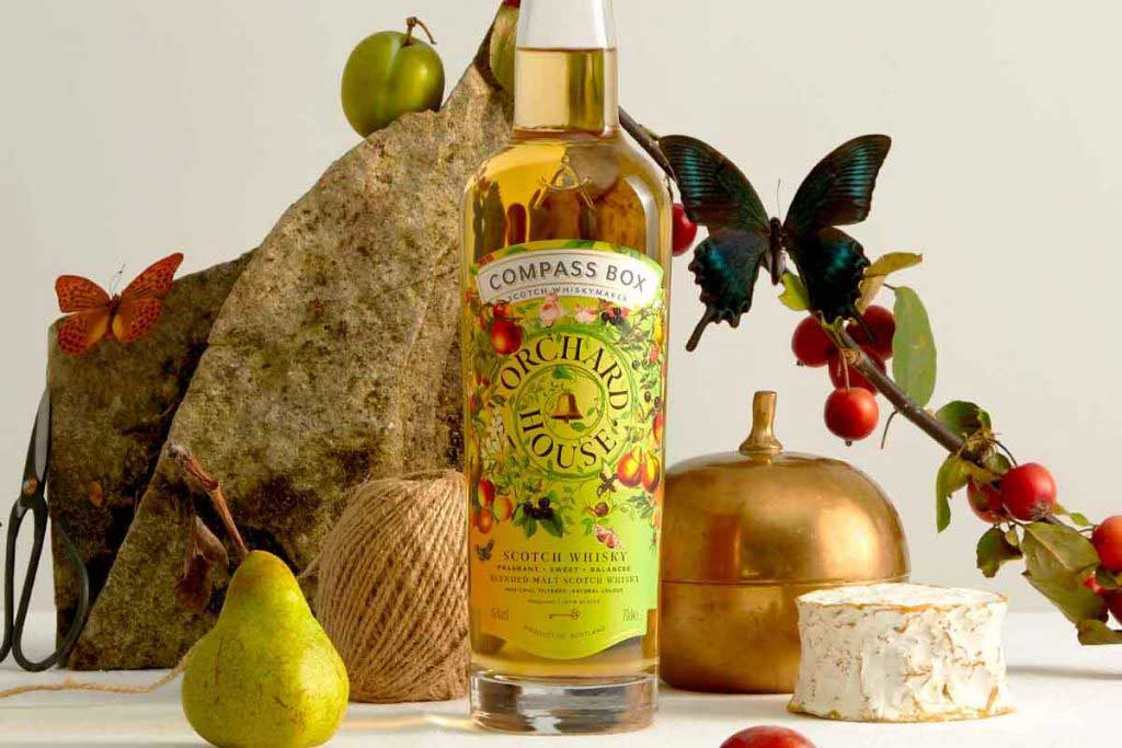 Bottle of Compass Box Orchard House blended malt Scotch whisky on table surrounded by fruit and cheese