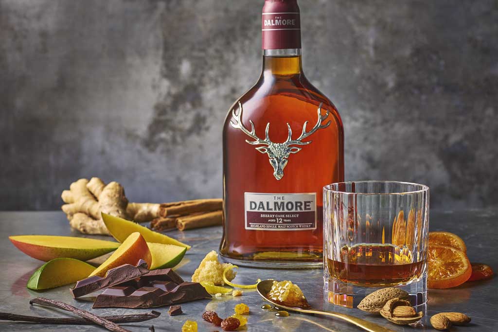 Bottle of Dalmore 12 single malt whisky on grey table surrounded by fruit and mixed spices