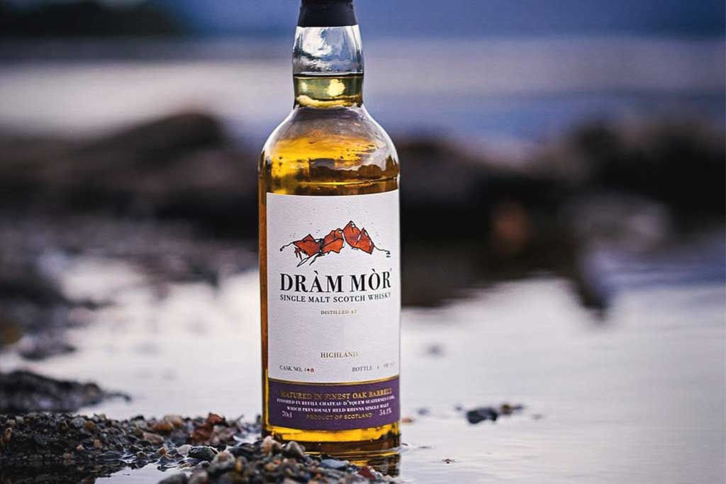 Bottle of Dràm Mòr Dumbarton single grain whisky sitting beside Scottish loch in water