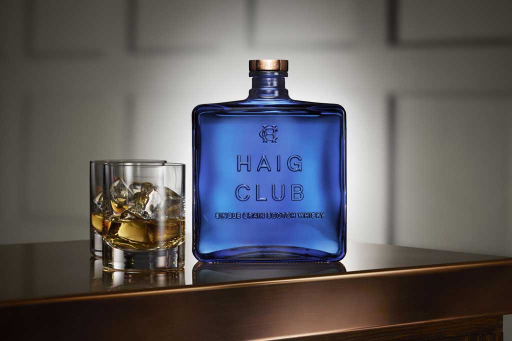 Bottle of Haig Club Whisky beside rocks drinking glass on wooden table top