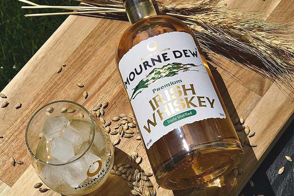 Bottle of Mourne Dew Single Malt Irish Whiskey outside on wooden table beside barley grains