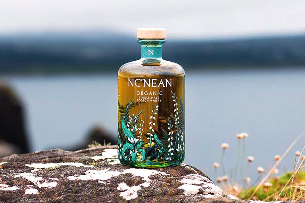 Bottle of Nc'nean Organic Single Malt Whisky on rocks in front of seascape