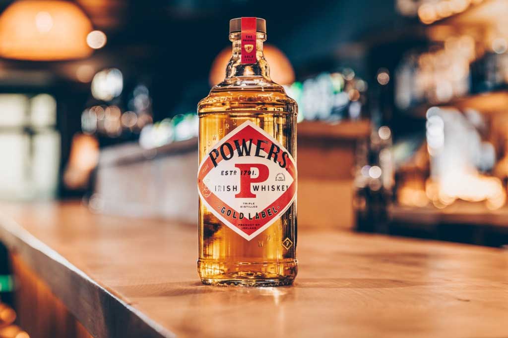 Bottle of Powers Gold Label Whiskey resting on wooden bar top