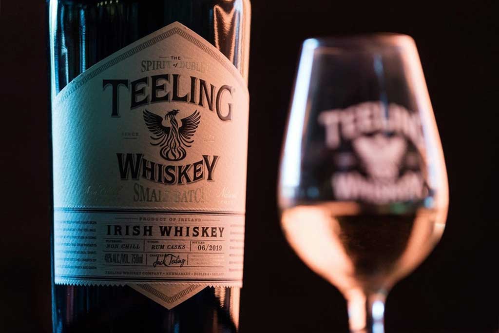 Bottle of Teeling Small Batch Whiskey beside Glencairn drinking glass in dark room