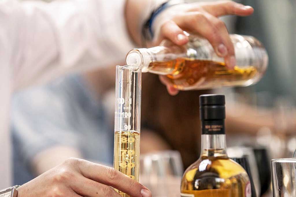 Person blending malt Scotch whisky in lab wearing white coat