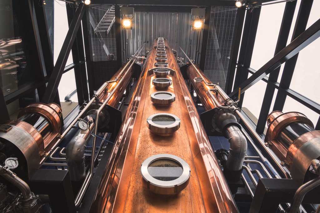 Upwards view of a tall copper column still inside a whiskey distillery