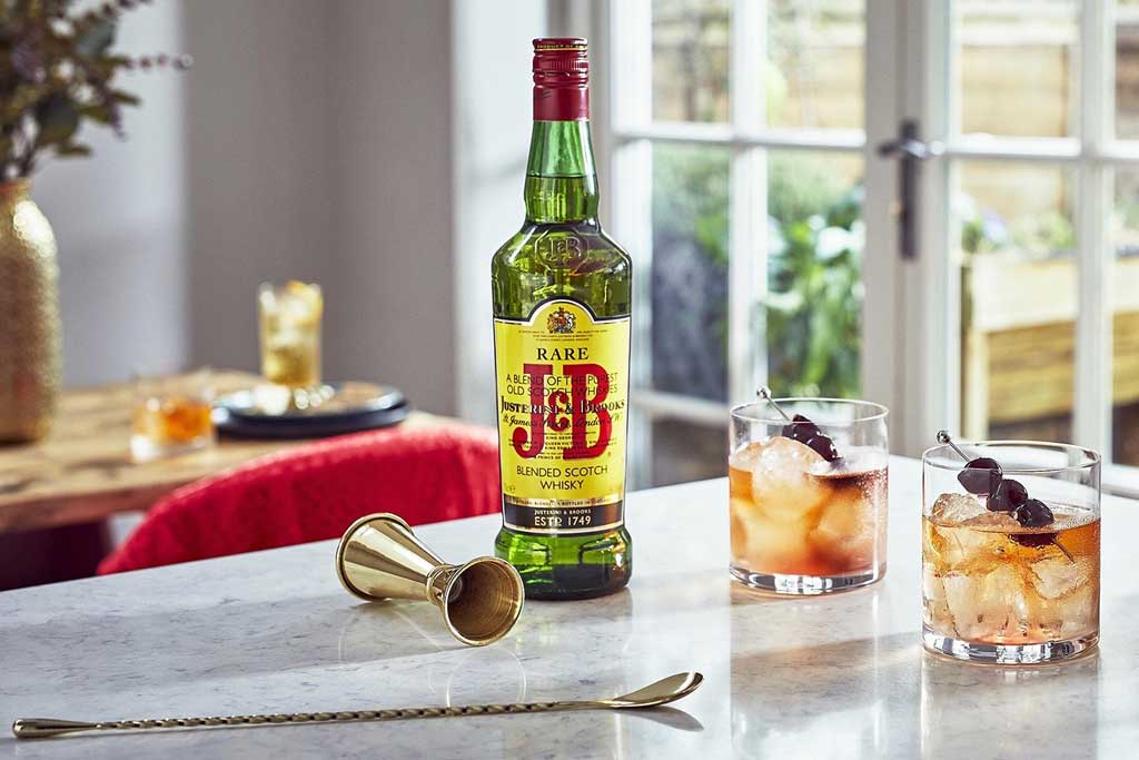 Bottle of J&B Rare blended Scotch whisky beside cocktail utensils on kitchen table