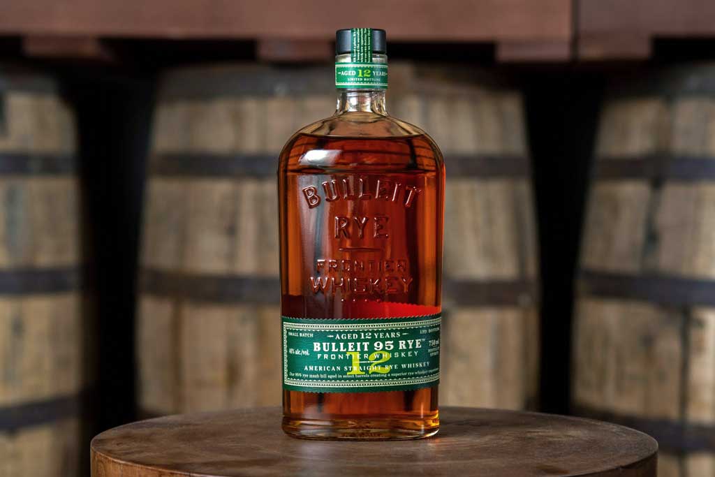 Bottle of Bulleit high rye bourbon whiskey on top of wooden barrel